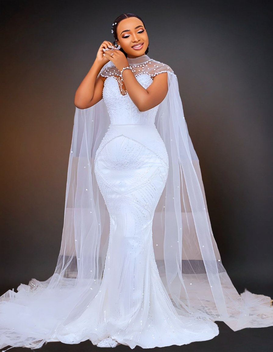 A stunning luxury wedding dress that features intricate beading and a long cape. It has a removable overskirt that adds versatility to the design.