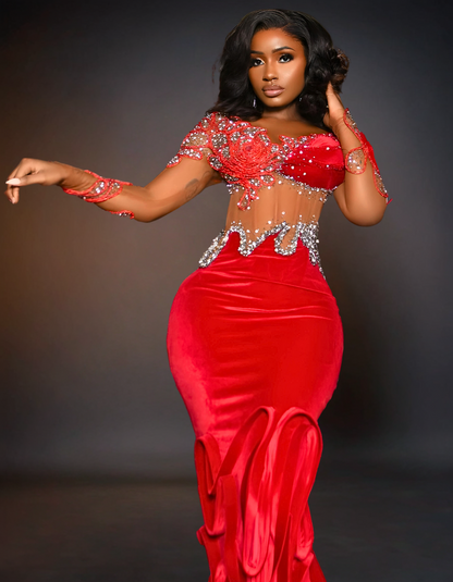 A luxury long red prom mermaid dress with a tail is displayed. The dress features a fitted bodice that flares out at the knees, creating a dramatic, elegant tail. 