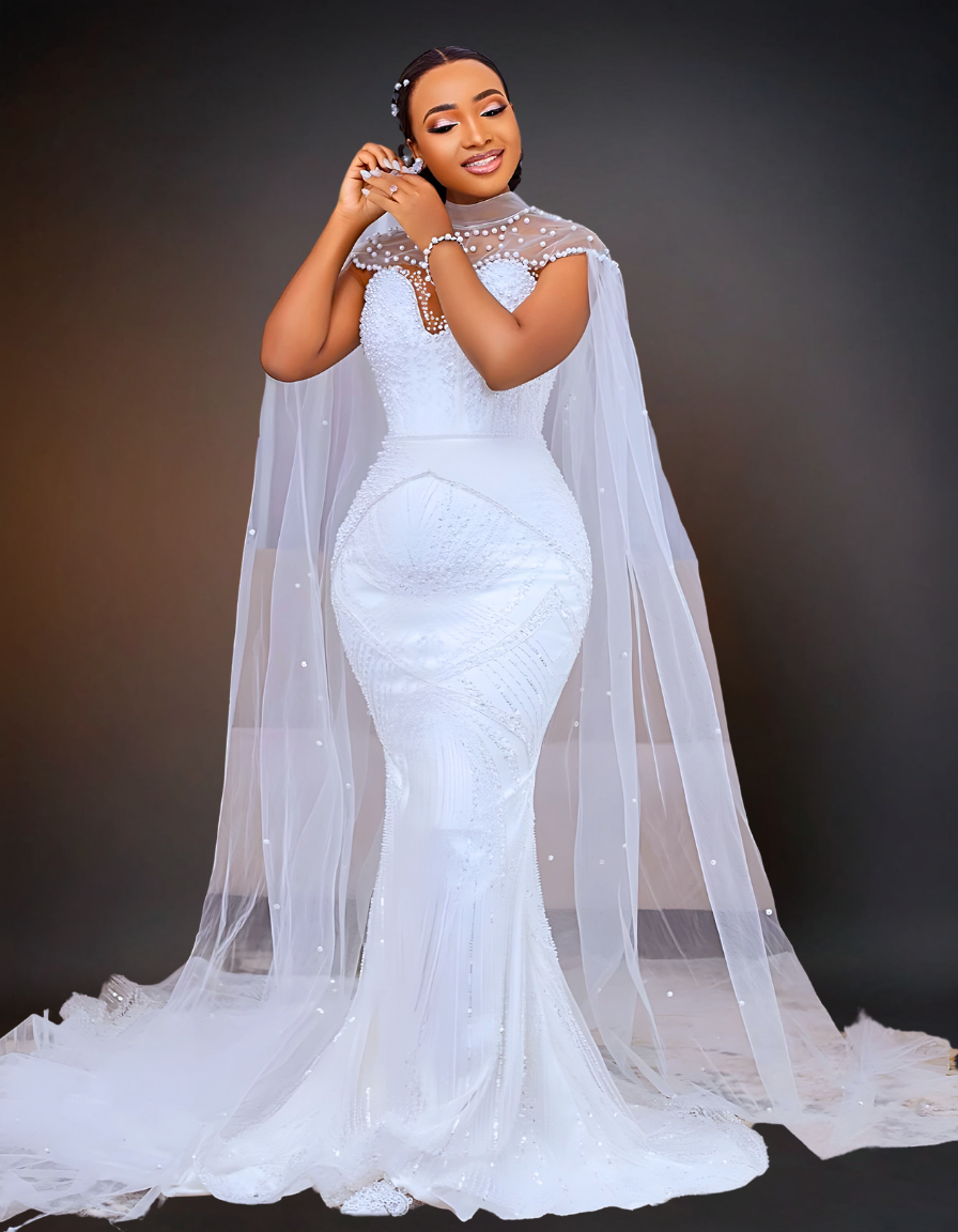  A stunning luxury wedding dress that features intricate beading and a long cape. It has a removable overskirt that adds versatility to the design. 