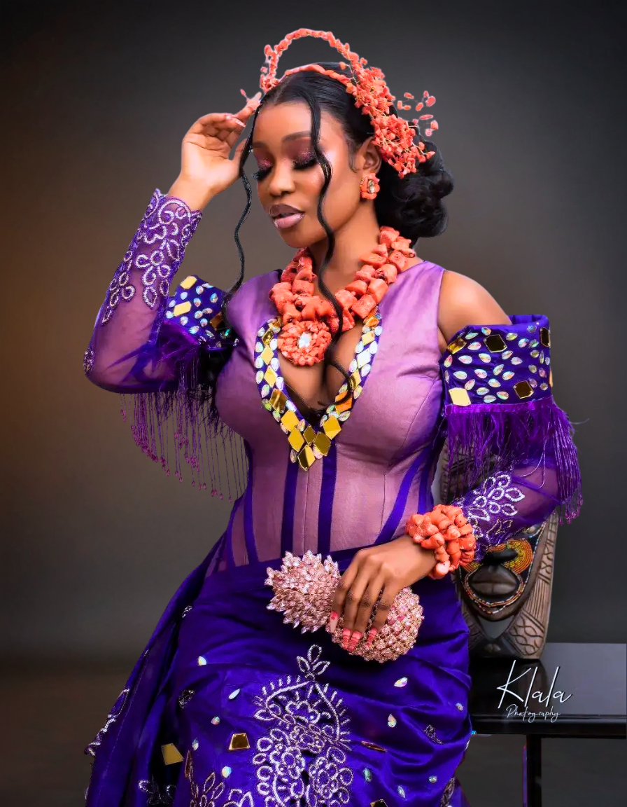 Woman in a purple traditional outfit with intricate designs and accessories against a dark background