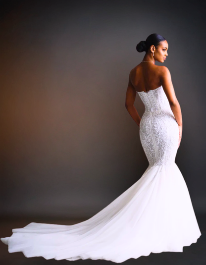 Woman in a white wedding dress with a long train against a dark background
